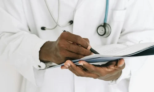 Professional doctor writing on a clipboard with a stethoscope in a medical office.