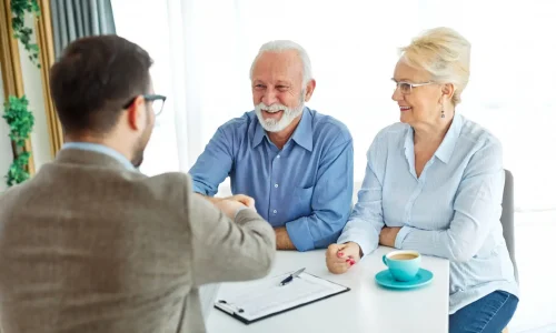 Portrait of a businessman or real estate agent or doctor shaking hands and signing a deal contract  with senior couple in his office